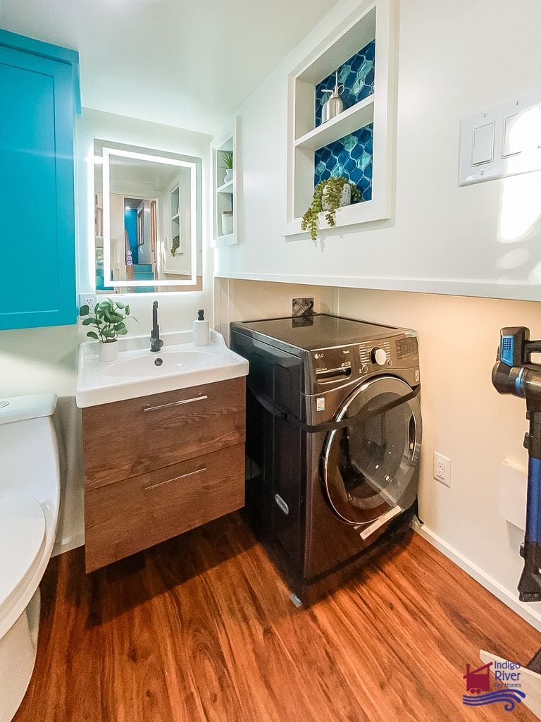 Hidden washer/dryer combo and cleaning storage tucked under the landing in the Entertainer tiny house.