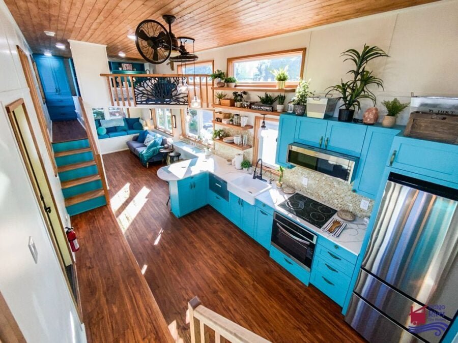 Bright turquoise cabinets and spacious galley kitchen inside the Tree House tiny home by Indigo River Tiny Homes.