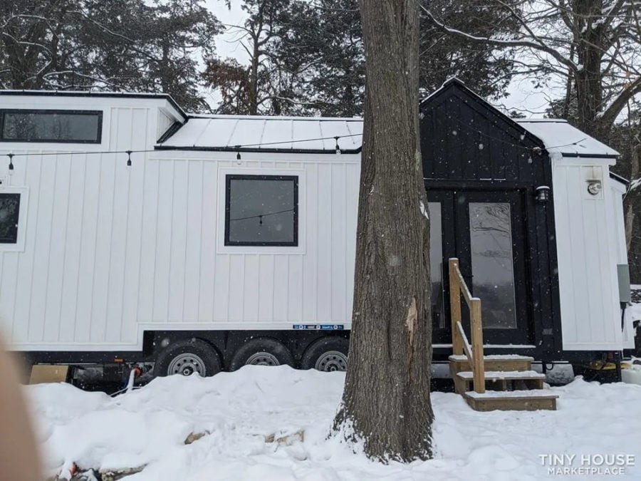 Rear angle of a 36-foot tiny house showing black metal roof and white siding