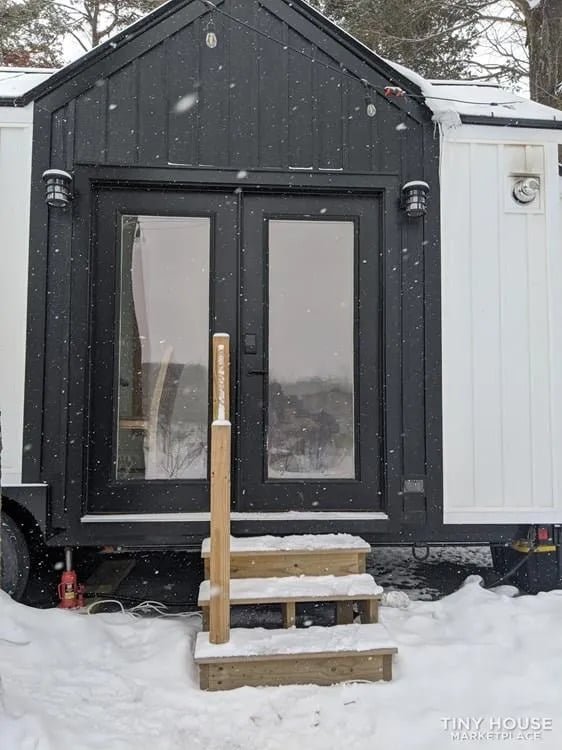 Modern tiny house exterior front angle showcasing large windows and metal roof